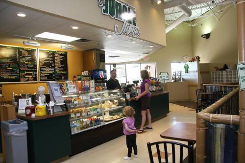 A cozy café interior with a counter displaying food and drinks, a customer ordering, and a child standing nearby.