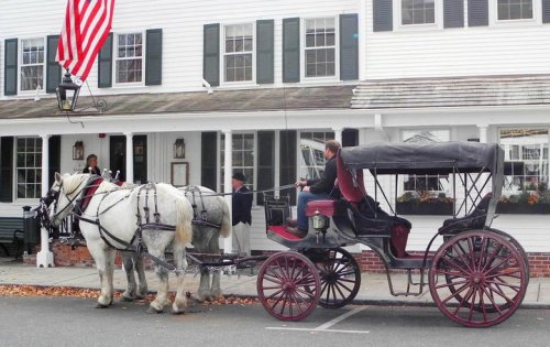 A horse-drawn carriage parked in front of a historic building with an American flag hanging above.