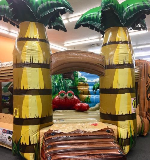 A colorful inflatable bounce house featuring palm trees and a red crab design, set in a playful indoor environment.