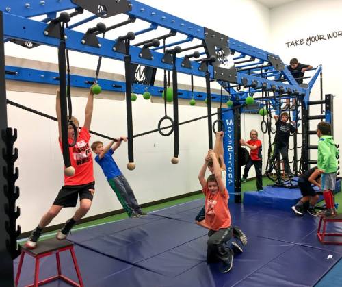 A group of children play on a colorful indoor gym setup with climbing equipment and mats.