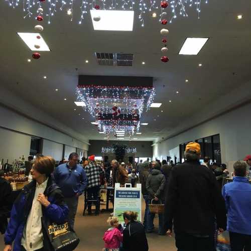 A bustling indoor market decorated with holiday lights and ornaments, filled with shoppers and festive displays.