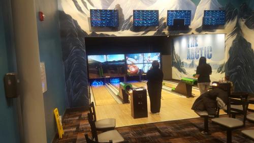 A bowling alley with a snowy mountain mural, featuring two people bowling and screens displaying scores.