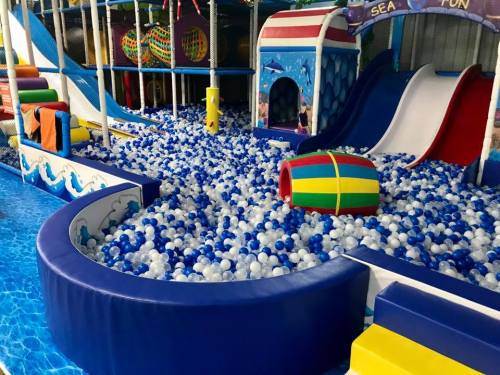 Colorful indoor play area featuring slides and a ball pit filled with blue and white balls.