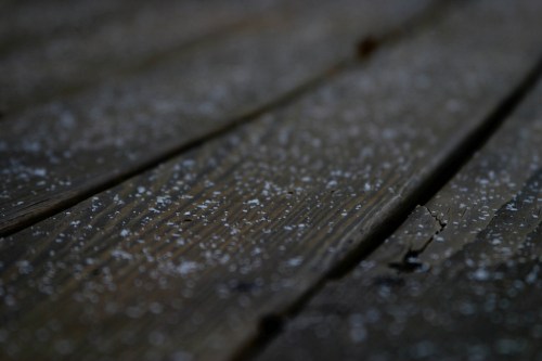 Close-up of a wooden surface covered in a light dusting of white particles, creating a textured, natural look.