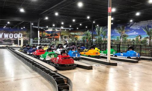 A colorful lineup of go-karts on a track in an indoor amusement center with a tropical mural in the background.