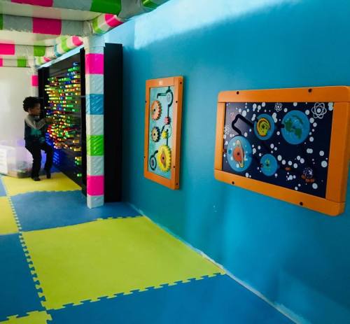 A colorful playroom with a child interacting with a light-up wall and two engaging activity boards.