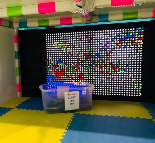 A colorful light peg box with a vibrant display of lights in a play area, surrounded by soft flooring.