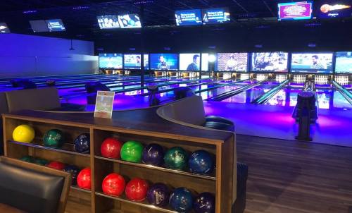 A bowling alley interior featuring colorful bowling balls and illuminated lanes with screens in the background.
