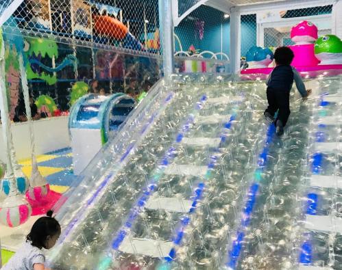 Two children play on a colorful, inflatable climbing structure in a vibrant indoor play area.