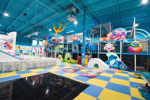 Bright indoor play area with colorful slides, climbing structures, and soft play mats for children.