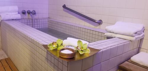 A serene spa setting featuring a tiled hot tub, fresh towels, and decorative flowers on a wooden tray.