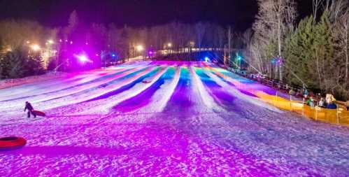 A snowy tubing hill at night, illuminated by colorful lights, with people enjoying the winter activity.