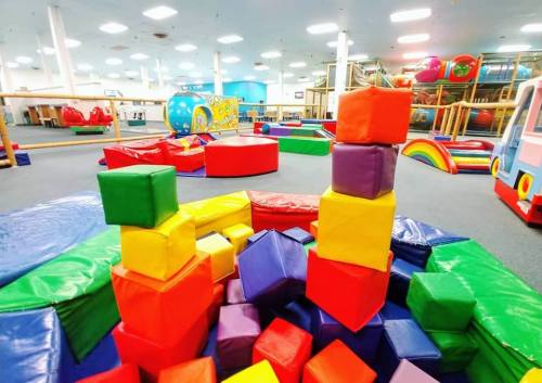 Colorful foam blocks stacked in a playful indoor gym filled with various soft play equipment and structures.
