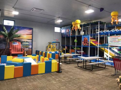 Indoor play area featuring colorful foam structures, slides, and tables in a spacious, well-lit environment.