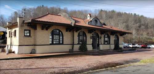 Historic building with a tiled roof, arched windows, and decorative elements, set against a wooded hillside.