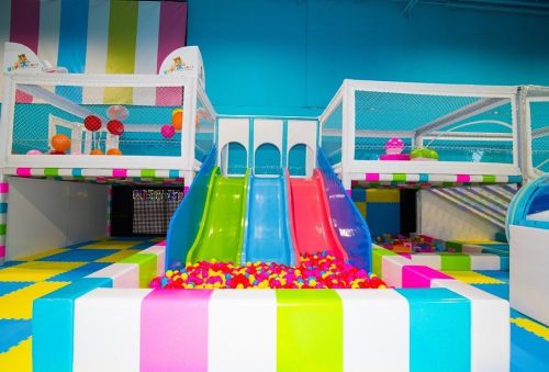 Colorful indoor play area featuring slides, ball pits, and climbing structures with bright, striped decor.