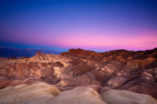 A stunning desert landscape at sunset, featuring layered mountains and a colorful sky in shades of purple and pink.