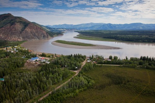 Aerial view of a winding river surrounded by lush greenery and mountains under a blue sky with scattered clouds.