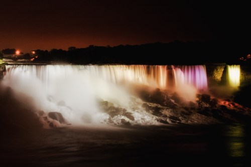 A illuminated waterfall at night, with colorful lights reflecting on the water and mist.