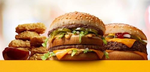Two burgers with sesame seed buns, cheese, lettuce, and condiments, alongside a pile of chicken nuggets and ketchup.