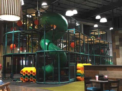 Indoor playground featuring a large green slide, climbing structures, and colorful play equipment.