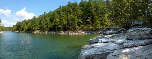 A serene lake surrounded by lush green trees and rocky shores under a clear blue sky.