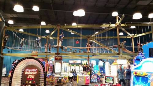 Indoor amusement center featuring a rope course above arcade games and colorful lights.