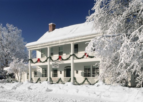 A charming inn covered in snow, adorned with festive garlands and red bows, surrounded by winter scenery.