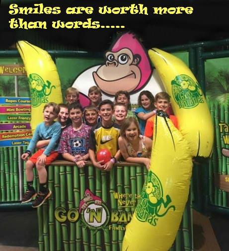 A group of children smiling together in a fun indoor play area, surrounded by inflatable banana decorations.