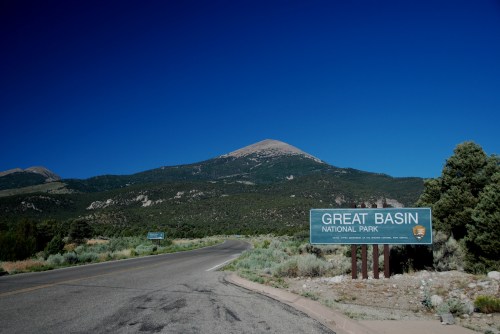 Sign for Great Basin National Park with a mountain backdrop under a clear blue sky. Road curves into the park.