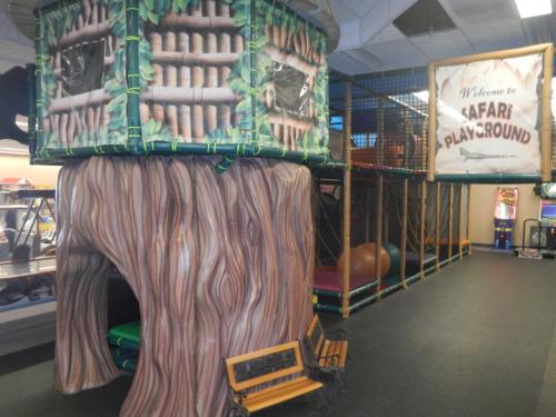 A colorful indoor playground featuring a treehouse structure and a sign welcoming visitors to "Safari Playground."