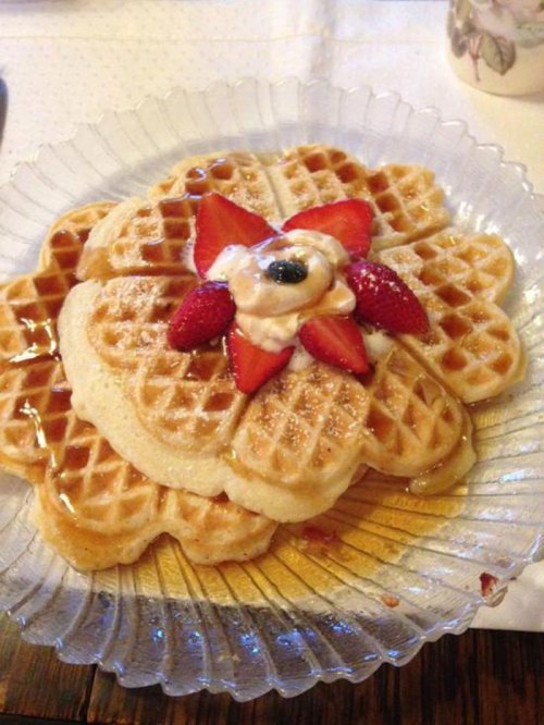 A plate of flower-shaped waffles topped with strawberries, cream, and syrup, served on a decorative glass dish.