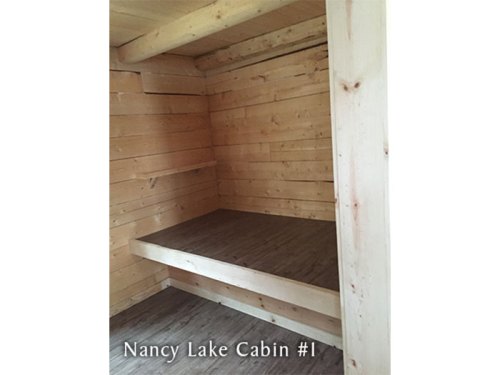 Interior of a wooden cabin with simple shelving and a raised platform, labeled "Nancy Lake Cabin #1."