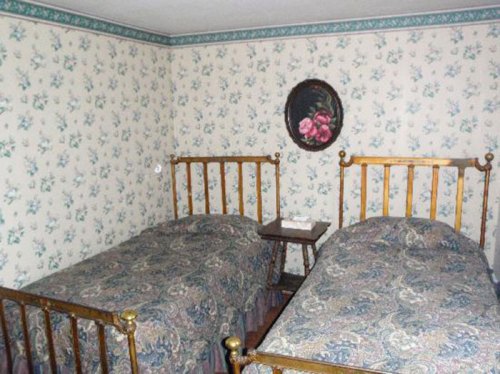 A cozy bedroom with two brass-framed beds, floral wallpaper, and a small nightstand between them.