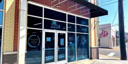 Exterior of a storefront with large glass windows, displaying "Open" sign and store hours. Address: 2214.