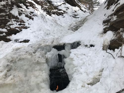 A snowy landscape with ice formations and a small flame visible in a cave-like opening.