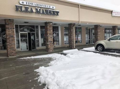 Snow covers the ground outside the Edwardsville Flea Market, with a white car parked nearby.