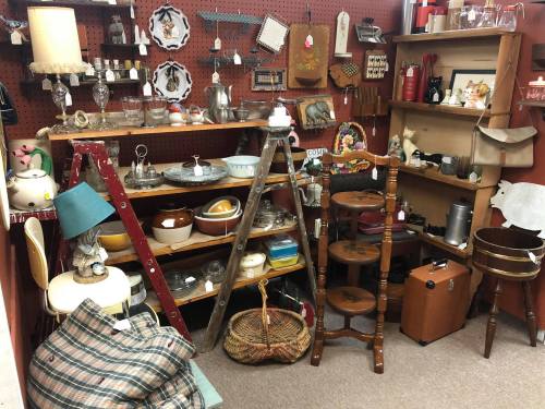A cozy antique shop display featuring shelves of vintage items, including dishes, decor, and furniture.