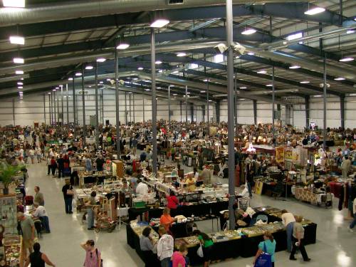 A large indoor market filled with numerous vendors and a crowd of people browsing various items.