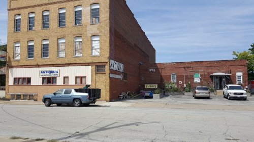 A brick building with a sign for "Antiques" and several parked cars in front on a sunny day.