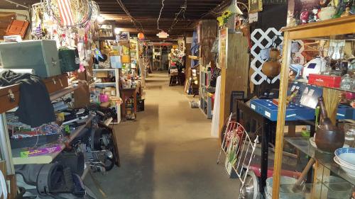 A cluttered basement filled with various items, including furniture, tools, and collectibles, creating a narrow walkway.