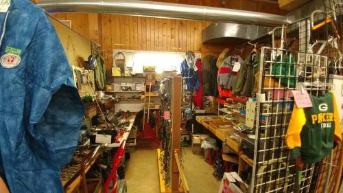 A cozy thrift store interior filled with clothing, shoes, and various items on wooden shelves and racks.