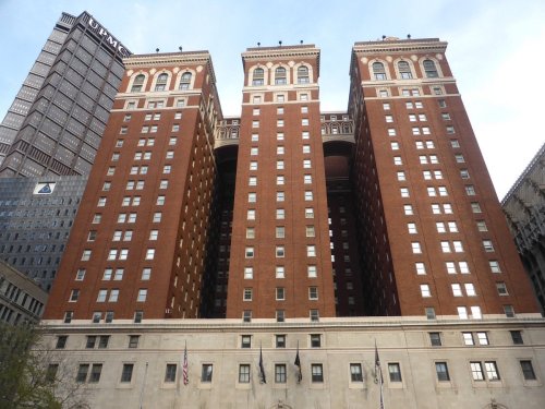Three tall brick buildings with ornate architecture, flanked by a modern skyscraper in an urban setting.