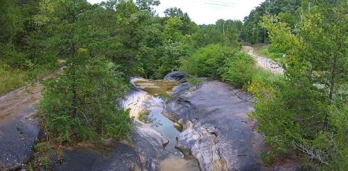 A rocky landscape with a shallow pool of water surrounded by lush green trees and shrubs.