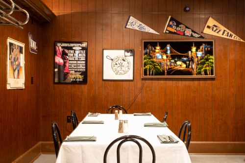 A cozy restaurant interior with a wooden wall, a table set for dining, and various framed artworks and pennants.