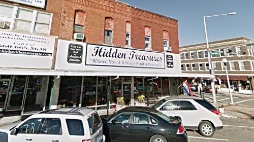 Storefront of "Hidden Treasures" with a sign reading "Where You'll Always Find A Treasure" and parked cars in front.