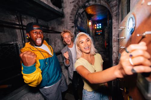 Three friends celebrate in a dimly lit room, one pressing a button while the others cheer excitedly.