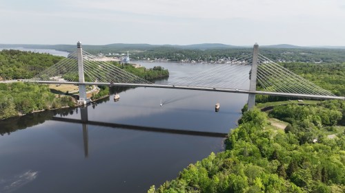 Aerial view of a cable-stayed bridge spanning a river, surrounded by lush greenery and distant hills.