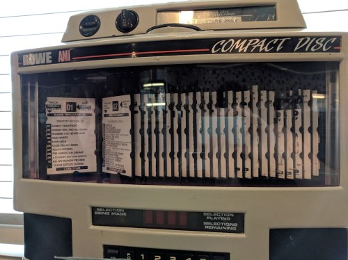 A vintage jukebox displaying a selection of compact discs and track listings.