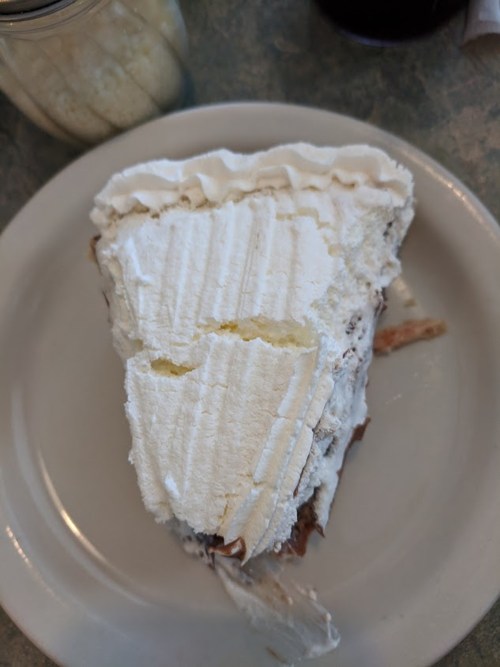 A slice of cake topped with whipped cream, served on a white plate with a jar in the background.